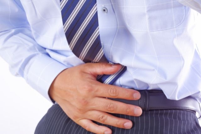 下腹部を押さえるスーツの男性