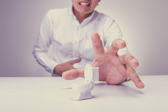 腹痛を感じ小さなトイレの模型に手を伸ばす男性