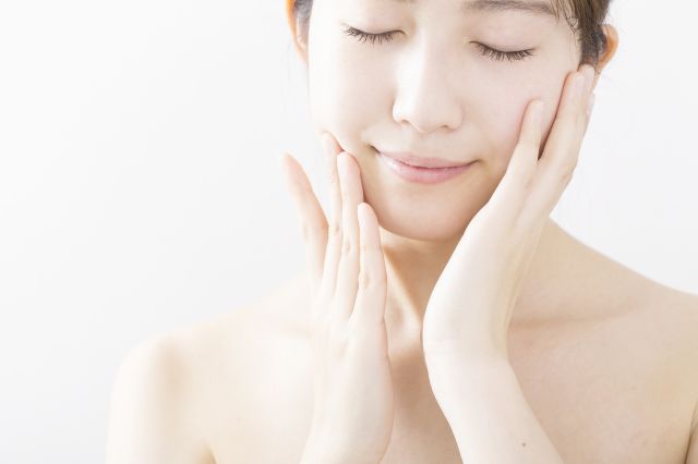 目をつむり頬のハリを気にする女性